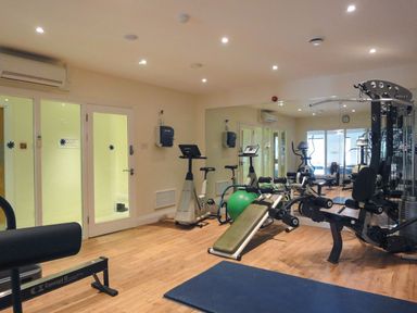A gym room with various exercise machines and equipment in front of a glass wall at 4 Burgh Island Causeway in Bigbury