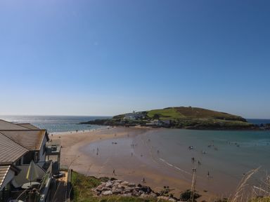 A beach with people walking and swimming near a grassy hill with buildings at 4 Burgh Island Causeway in Bigbury