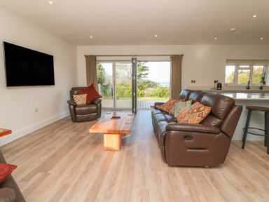 A living room with brown leather sofas a wooden coffee table a wall mounted tv and sliding glass doors opening to a garden at Linden View in Combe Martin