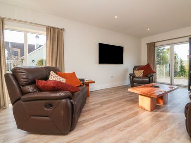 A living room with leather sofas wooden coffee table and wall-mounted television at Linden View in Combe Martin