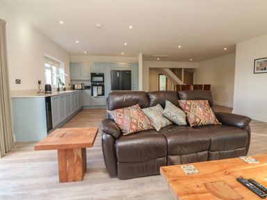 An open plan kitchen and living room with a brown leather sofa with patterned cushions a wooden coffee table and side table at Linden View in Combe Martin