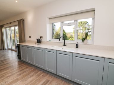 A kitchen with blue cabinets a white countertop a black faucet and a window with a view at Linden View in Combe Martin