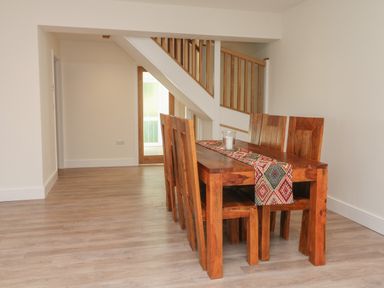 A dining area with a wooden table and six chairs under a staircase at Linden View in Combe Martin