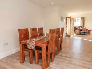 A dining area with a wooden table and six chairs with a patterned table runner in an open plan room with a brown leather armchair in Linden View Combe Martin