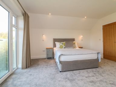 A bedroom with a double bed bedside tables gray carpet and a wooden door at Linden View in Combe Martin