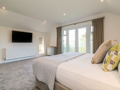A bedroom with a bed and pillows a wall-mounted TV a chest of drawers and windows at Linden View in Combe Martin