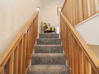 A carpeted staircase with wooden railings and a cushioned armchair at Linden View in Combe Martin