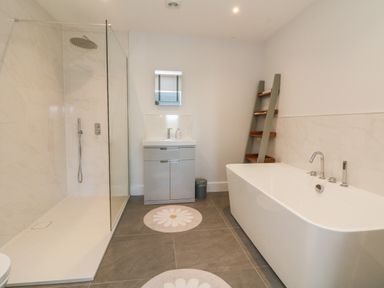 A bathroom with a walk-in shower, sink with cabinet, freestanding bathtub, ladder shelf, and floral rugs at Linden View in Combe Martin