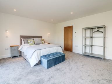 A bedroom with a bed pillows a blue bench a wooden door a gray nightstand and an open wardrobe at Linden View in Combe Martin