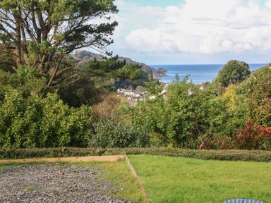A garden with grass and gravel area overlooking trees houses and the sea at Linden View in Combe Martin