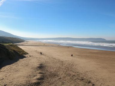 A wide sandy beach with a few people walking near the shore and dunes on the left at Linden View in Combe Martin