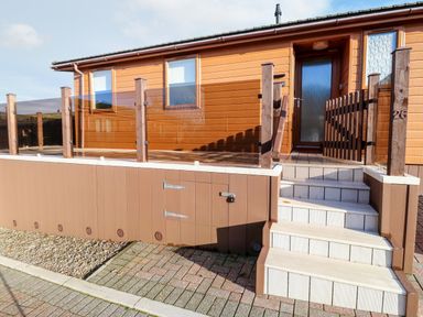 An exterior view of a brown mobile home with stairs leading to a porch enclosed by a glass railing at Serenity Sunset in Ilfracombe