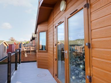 A balcony with glass railing outside wooden cabins in a row at Serenity Sunset in Ilfracombe
