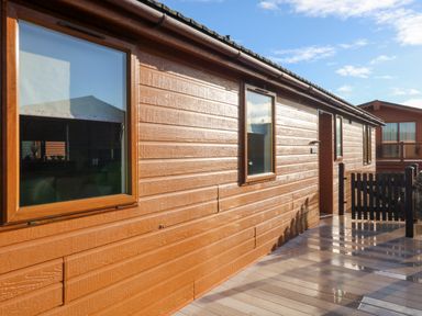Exterior view of a wooden house with windows and a door leading to a wooden deck with a black gate at Serenity Sunset in Ilfracombe