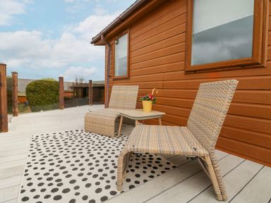 An outdoor deck with two wicker chairs a small table with a potted plant and a polka dot rug at Serenity Sunset in Ilfracombe