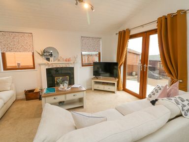 A living room with sofas a coffee table a television and large windows with curtains at Serenity Sunset in Ilfracombe