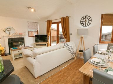 A living room with a sofa TV coffee table dining table and chairs at Serenity Sunset in Ilfracombe