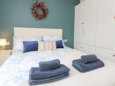 A bedroom with a bed with blue and white bedding towels placed on the bed and a white wardrobe against a blue wall at Serenity Sunset Ilfracombe