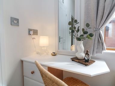 A corner desk with a lamp a vase with greenery and a small sculpture near a window with curtains at Serenity Sunset in Ilfracombe