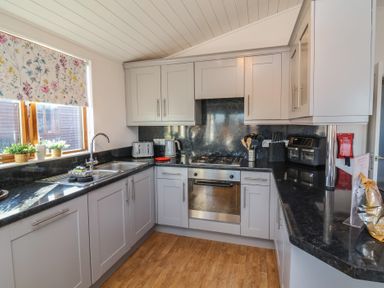 A kitchen with grey cabinets black countertops and wooden floor at Serenity Sunset in Ilfracombe