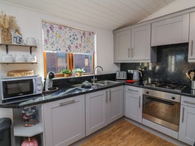 A kitchen with grey cabinets black countertop microwave and oven at Serenity Sunset in Ilfracombe
