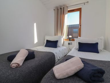 A bedroom with two single beds each with pillows and folded towels by a window at Serenity Sunset in Ilfracombe