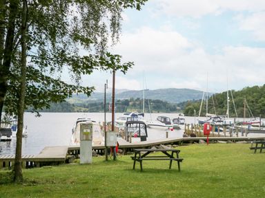 A grassy area with picnic tables near a wooden dock with boats on a lake at Tranquil Waters in Lakeside 16 White Cross Bay near Windermere