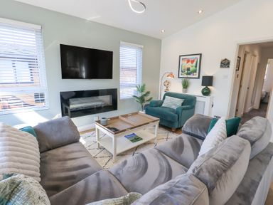 A living room with a gray sectional sofa a green armchair a white coffee table and a wall-mounted TV at Tranquil Waters Lakeside 16 White Cross Bay near Windermere