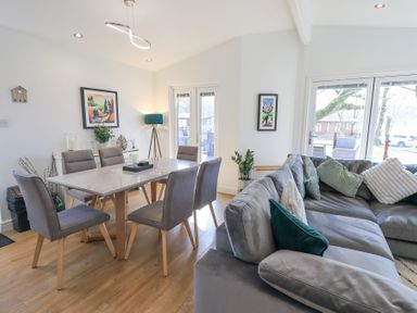 A dining area with a table and chairs next to a living room with a large sofa and cushions at Tranquil Waters in Lakeside 16 White Cross Bay near Windermere