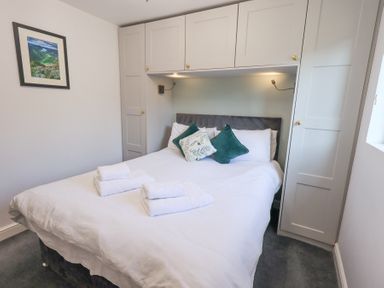 A bedroom with a double bed pillows towels overhead cabinets and a framed picture on the wall at Tranquil Waters Lakeside 16 White Cross Bay near Windermere