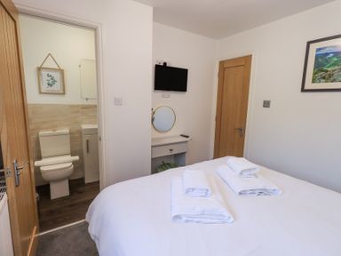 A bedroom with a bed folded towels a door leading to a bathroom and a TV on the wall at Tranquil Waters Lakeside 16 White Cross Bay near Windermere