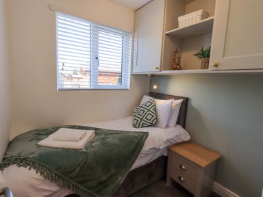 A small bedroom with a single bed green blanket pillows a bedside table and wall cabinets at Tranquil Waters in Lakeside 16 White Cross Bay near Windermere