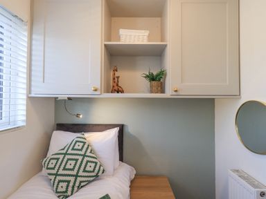 A small bedroom with a single bed green and white patterned cushion wooden side table and overhead cabinets at Tranquil Waters Lakeside 16 White Cross Bay near Windermere