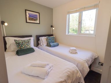 A bedroom with two single beds white linens folded towels and a window at Tranquil Waters Lakeside 16 White Cross Bay near Windermere