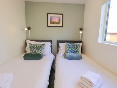 A bedroom with two single beds with cushions and rolled towels by a window at Tranquil Waters Lakeside 16 White Cross Bay near Windermere
