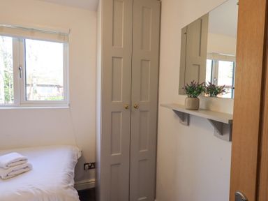 A bedroom with a bed with folded towels next to a window and a corner cupboard with a mirror and shelf holding a plant at Tranquil Waters in Lakeside 16 White Cross Bay near Windermere