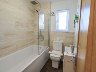 A bathroom with a bathtub shower combination a toilet and a small sink with a window at Tranquil Waters Lakeside 16 White Cross Bay near Windermere