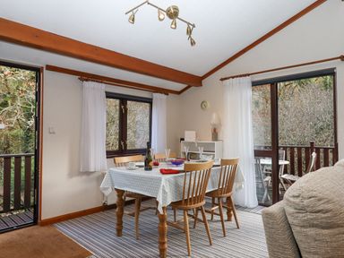 A dining room with a table set for four near windows and a sliding door at Teign River Retreat in Drewsteignton near Moretonhampstead