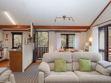 An open living space with sofas, dining table, kitchen area, and large windows with curtains at Teign River Retreat Drewsteignton near Moretonhampstead
