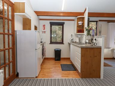 A kitchen with white cabinets refrigerator sink coffee machine and window at Teign River Retreat in Drewsteignton near Moretonhampstead
