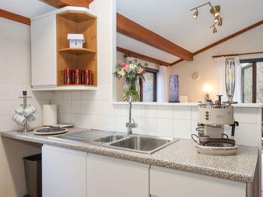 A kitchen counter with a sink a coffee maker red canisters and flowers at Teign River Retreat Drewsteignton near Moretonhampstead