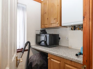 A small utility room with a microwave on a countertop wooden cabinets and a vacuum cleaner near a window at Teign River Retreat in Drewsteignton near Moretonhampstead