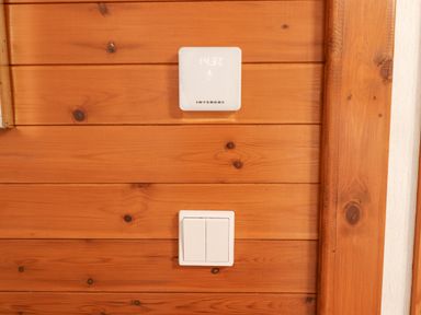 A wooden wall with a digital thermostat showing temperature and a double light switch at Teign River Retreat in Drewsteignton near Moretonhampstead