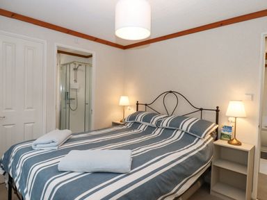 A bedroom with a striped bedspread two bedside lamps and an ensuite shower at Teign River Retreat in Drewsteignton near Moretonhampstead