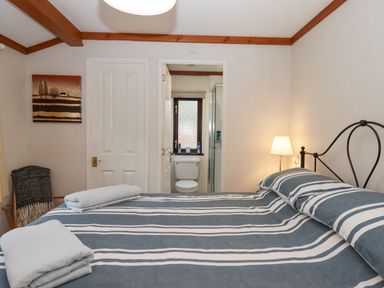 A bedroom with a bed striped bedding lamp and an en suite bathroom at Teign River Retreat Drewsteignton near Moretonhampstead