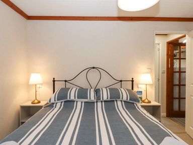A bedroom with a bed with blue and white striped bedding two bedside tables with lamps and a door leading to a hallway at Teign River Retreat in Drewsteignton near Moretonhampstead