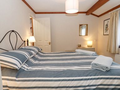 A bedroom with a double bed with striped bedding bedside lamps a mirror and a framed picture at Teign River Retreat in Drewsteignton near Moretonhampstead