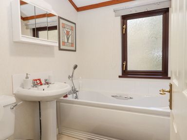 A bathroom with a bathtub a sink and a toilet a window with frosted glass and a wall mirror above the sink at Teign River Retreat in Drewsteignton near Moretonhampstead