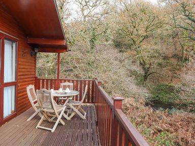 A wooden balcony with a round table and four chairs overlooking trees and a small stream at Teign River Retreat in Drewsteignton near Moretonhampstead
