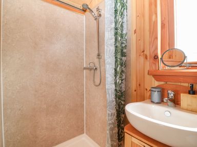 A shower area with a showerhead and a sink with a mirror on wooden walls at Hafan Gelli Sheperds Hut - Enlli in Pwllheli